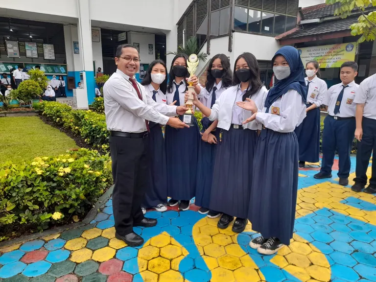 Guru dan kelompok siswa berfoto bersama memegang piala