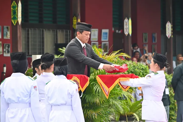 Penyerahan bendera kepada petugas pengibar dalam upacara di halaman sekolah